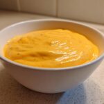 Close-up of a white bowl filled with creamy, bright orange nacho cheese sauce.