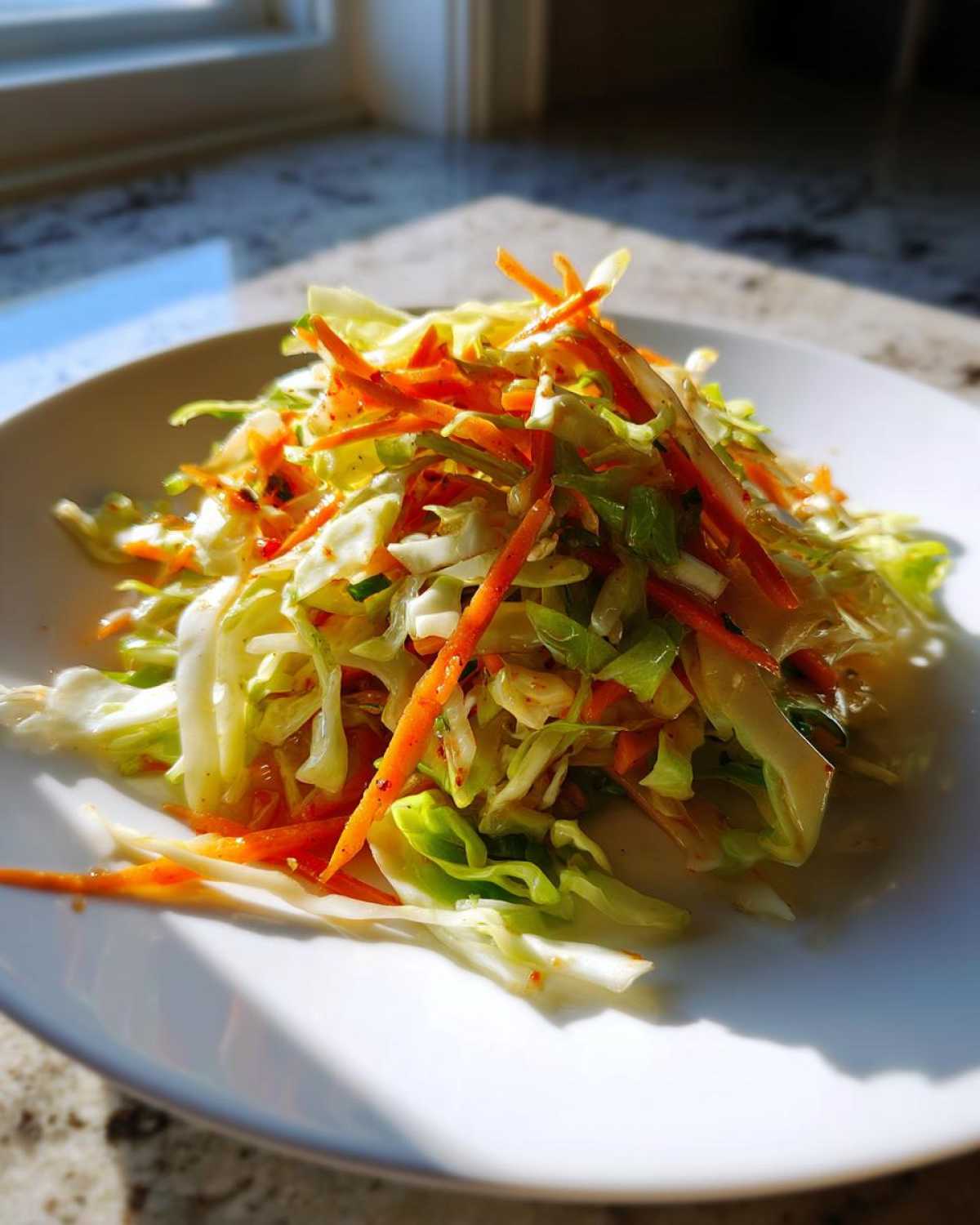 A bright, close-up serving of fresh cabbage salad mixed with shredded carrots on a white plate.
