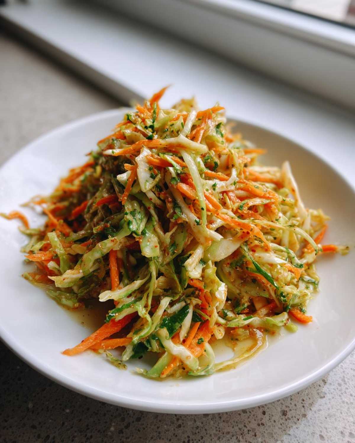 A mound of fresh, shredded cabbage salad mixed with bright orange carrots on a white plate.