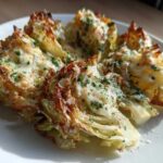 Four wedges of baked cabbage recipe topped with melted cheese and fresh parsley on a white plate.