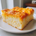 A square slice of rich, moist cassava cake with shredded coconut texture and a golden, baked cheese topping.
