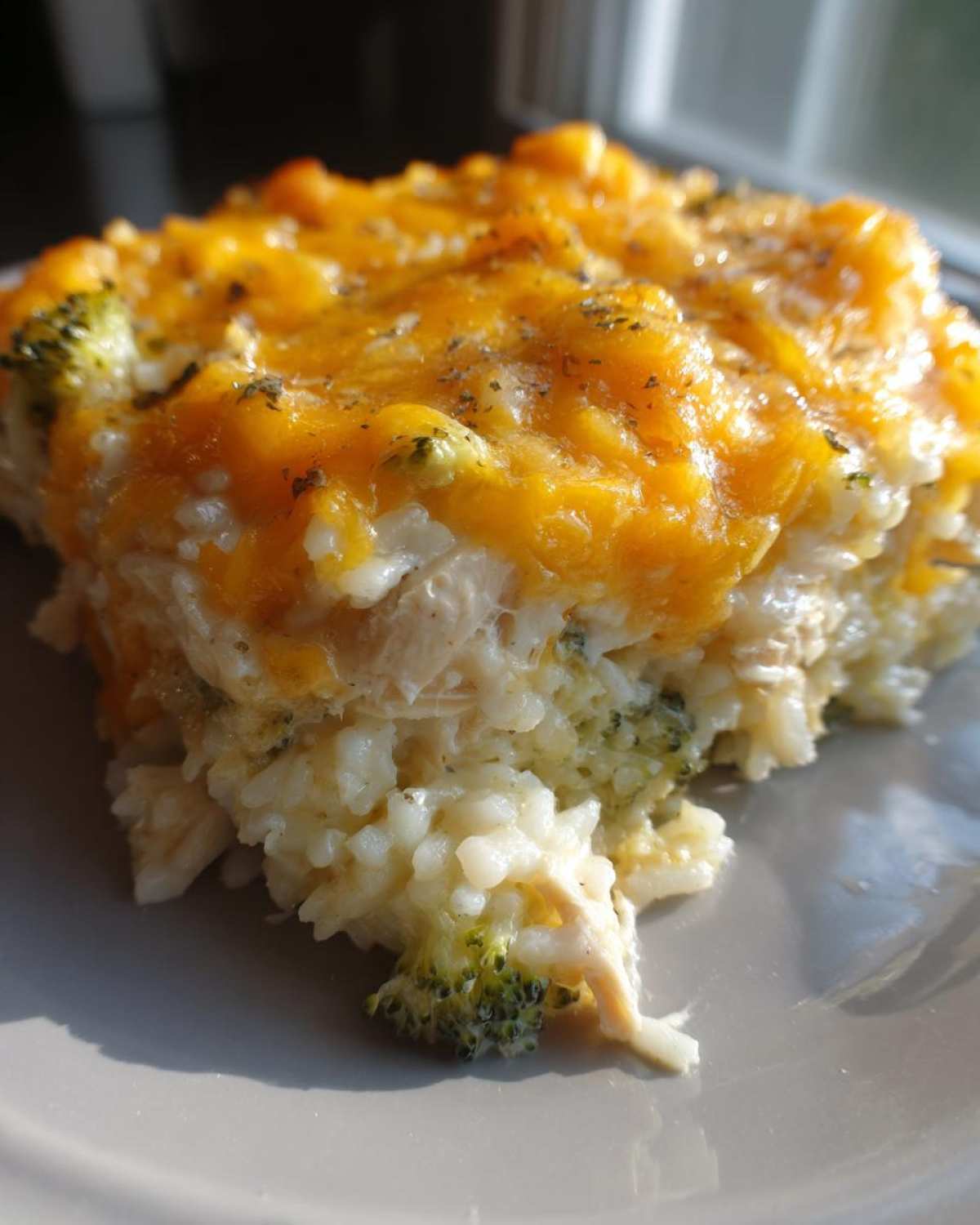 A close-up serving of cheesy chicken and rice casserole, topped with melted cheddar cheese and broccoli florets.