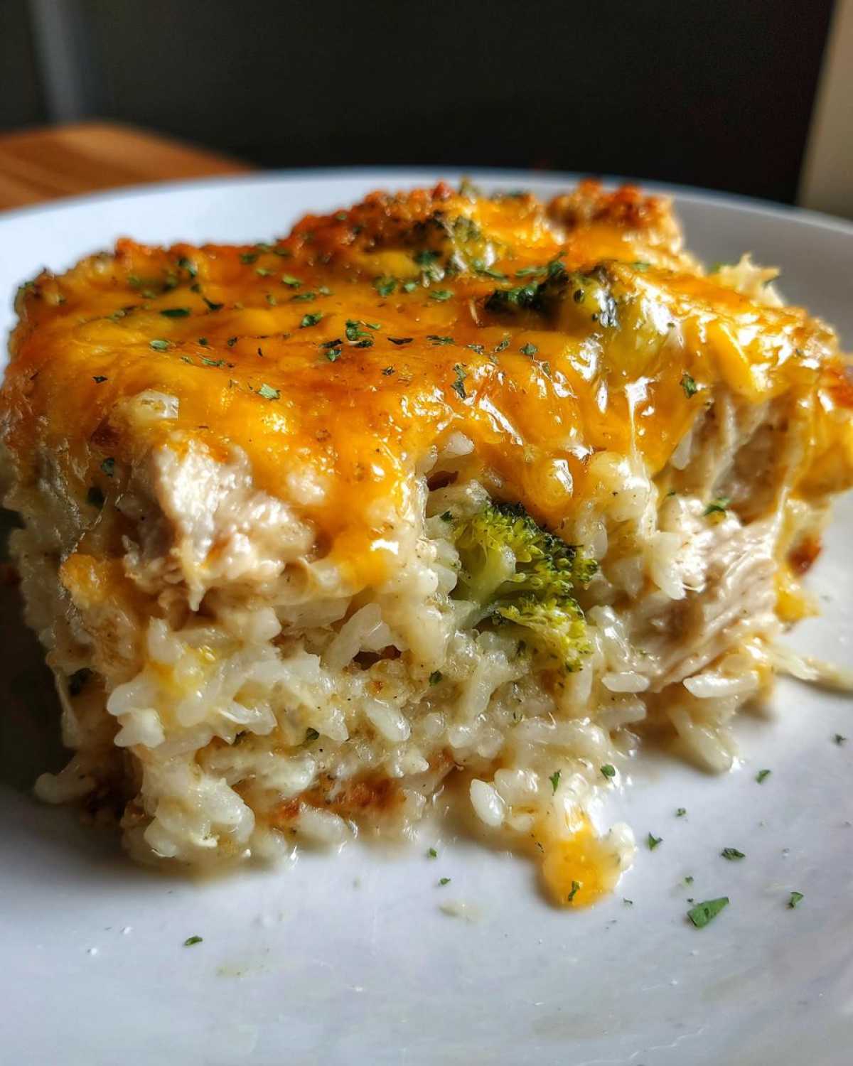 Close-up of a serving of cheesy chicken and rice casserole topped with melted cheddar and parsley.