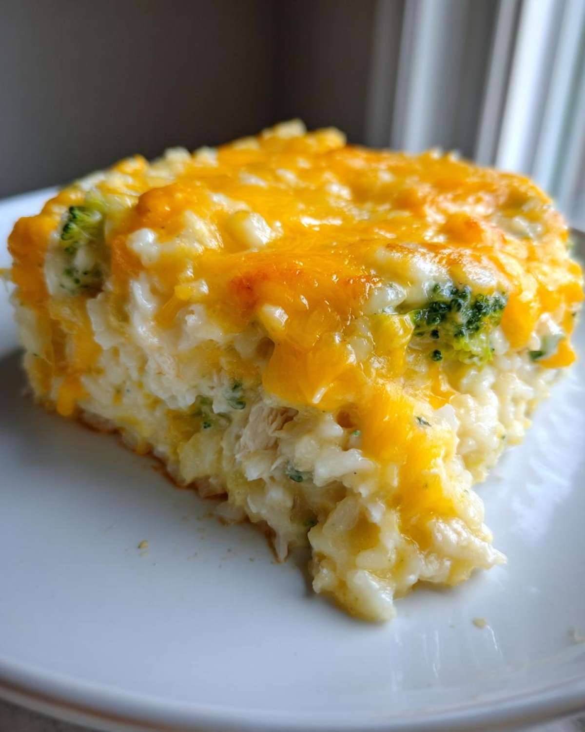 A close-up serving of cheesy chicken and rice casserole topped with melted cheddar cheese and visible broccoli florets.