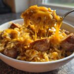Fork lifting a cheesy portion of sausage and rice, showing melted cheese stretching from the bowl.
