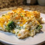 A close-up serving of creamy chicken broccoli rice casserole topped with melted cheddar and crispy breadcrumbs.