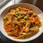 A close-up bowl filled with savory chicken chow mein recipe noodles, chicken pieces, carrots, and cabbage.
