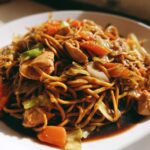 Close-up of a serving of saucy chicken chow mein recipe with noodles, chicken pieces, carrots, and cabbage.
