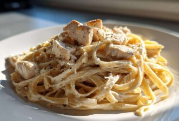 A close-up serving of creamy chicken fettuccine alfredo pasta topped with seasoned chicken pieces.