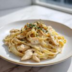 A serving of rich chicken fettuccine alfredo pasta topped with fresh parsley and black pepper.