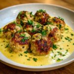 Close-up of seared chicken piccata meatballs served in a creamy lemon-caper sauce and garnished with fresh parsley.