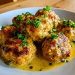 Close-up of several golden-brown chicken piccata meatballs served in a bright lemon-caper sauce, garnished with fresh parsley.