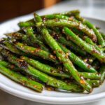 Vibrant close-up of glossy, stir-fried chinese green beans with garlic sauce coating.