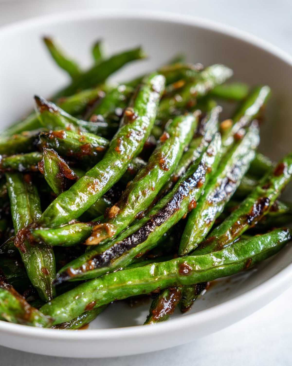 Close-up of bright green, blistered chinese green beans with garlic sauce in a white bowl.