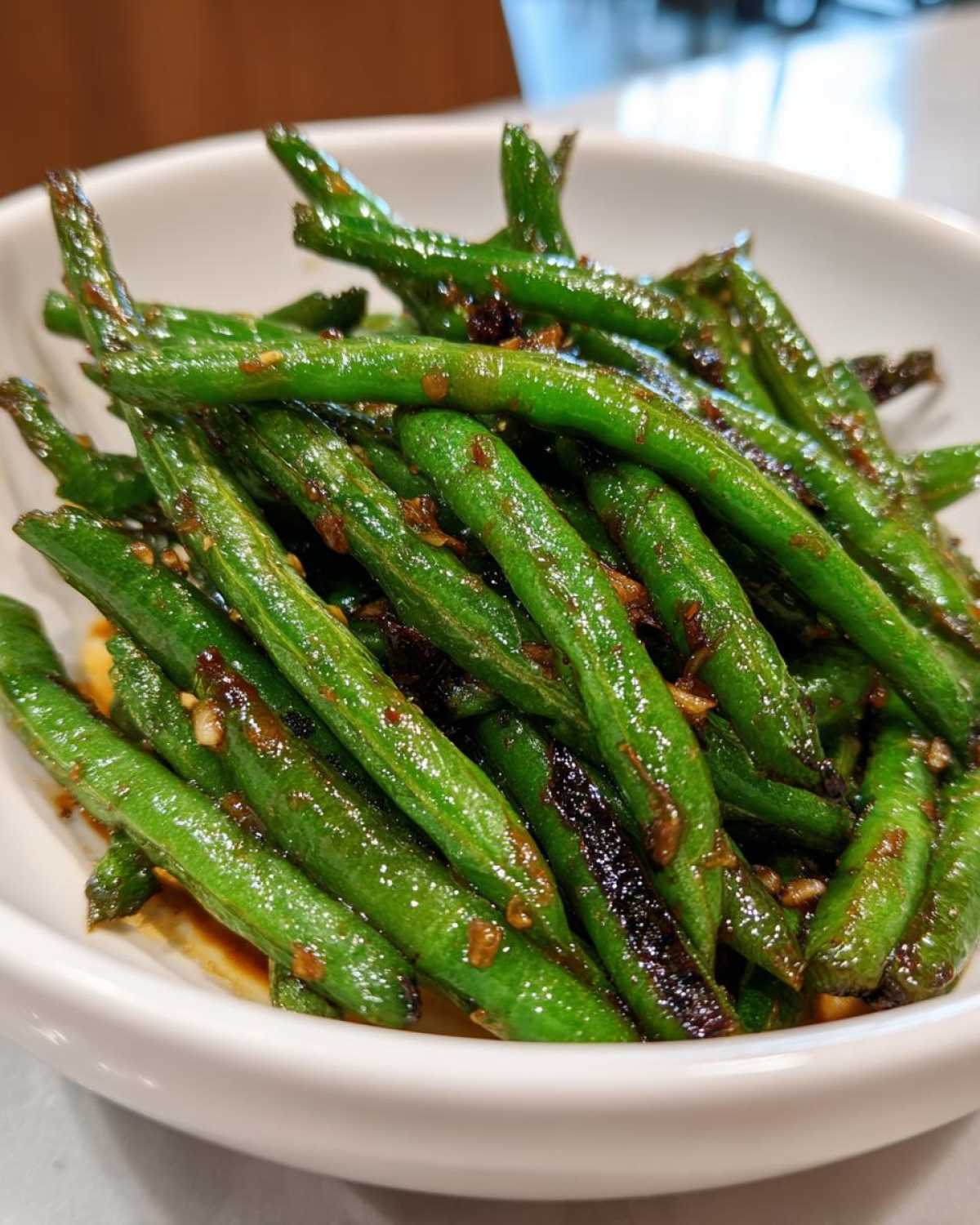 Close-up of bright green, glossy chinese green beans with garlic sauce in a white serving bowl.