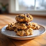A stack of four homemade chocolate chip breakfast cookie sits on a light plate, illuminated by sunlight.