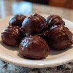 A close-up of several rich, chocolate-covered Oreo balls stacked on a white plate.