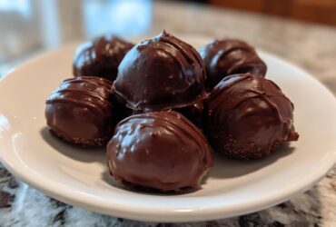 A close-up of several rich, chocolate-covered Oreo balls stacked on a white plate.