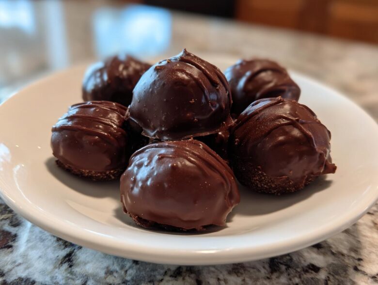 A close-up of several rich, chocolate-covered Oreo balls stacked on a white plate.