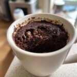 Close-up of a rich chocolate mug cake baked in a white mug, topped with melted chocolate chips.