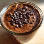 Close-up overhead view of rich chocolate overnight oats in a glass jar, topped generously with mini chocolate chips.