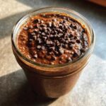 Close-up of rich chocolate overnight oats in a glass jar, topped generously with mini chocolate chips.