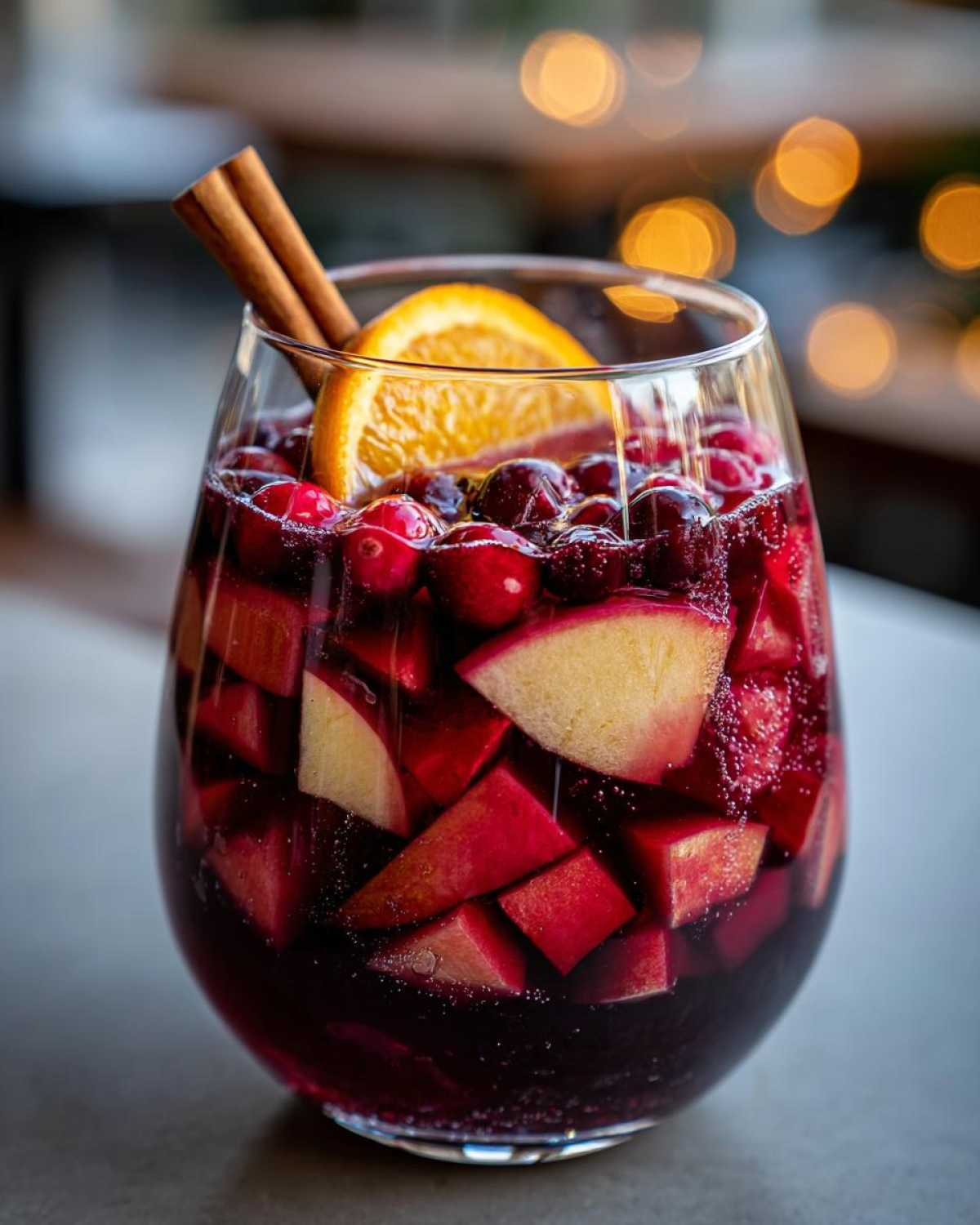 Close-up of a glass filled with rich red Christmas sangria, loaded with apples, cranberries, and garnished with an orange slice and cinnamon sticks.
