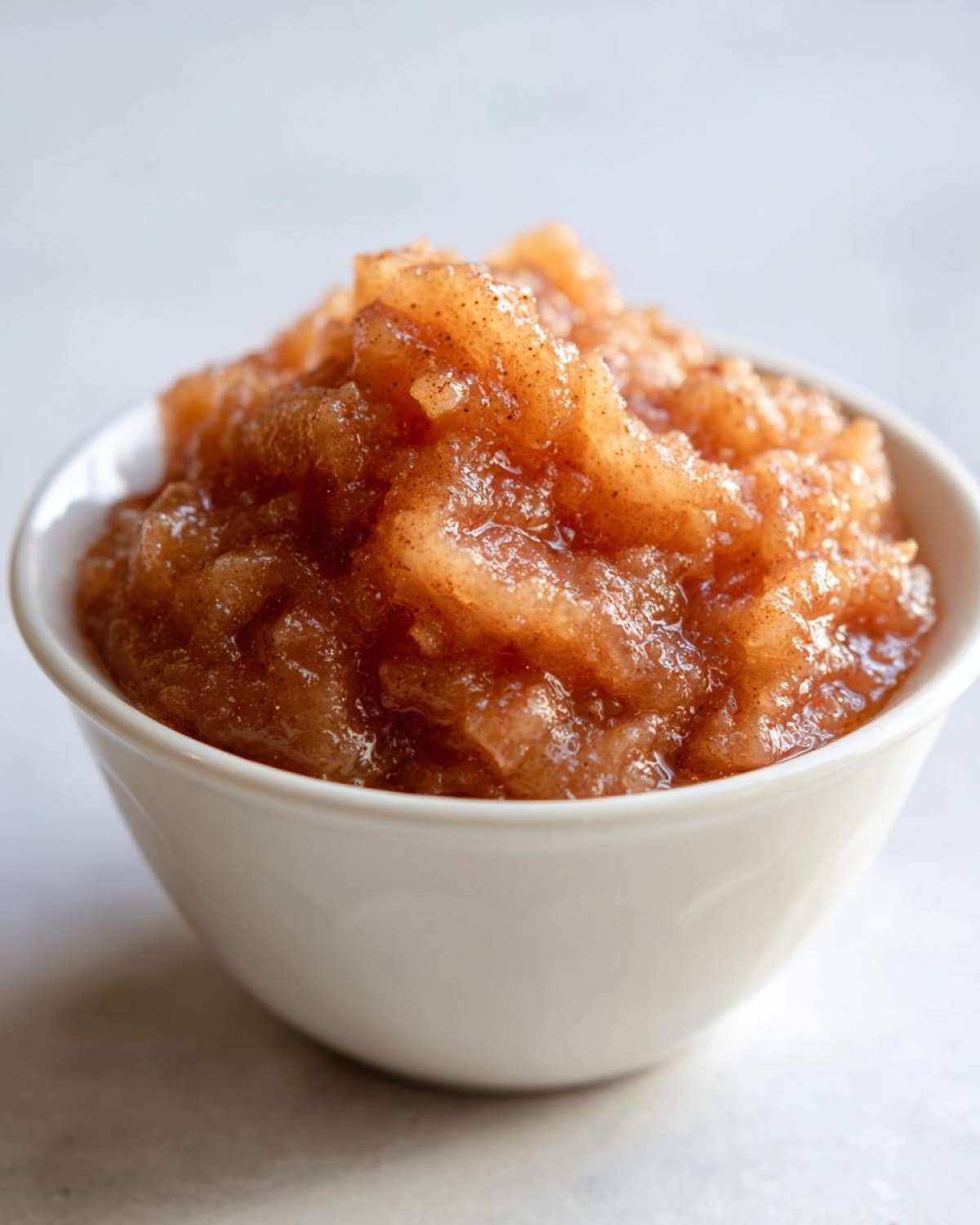 Close-up of chunky, homemade applesauce seasoned with cinnamon served in a small white bowl.