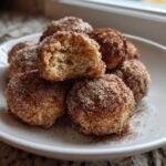 A stack of freshly made cinnamon sugar snowball cookies, one broken open showing the soft interior.