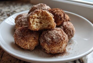 A stack of freshly made cinnamon sugar snowball cookies, one broken open showing the soft interior.