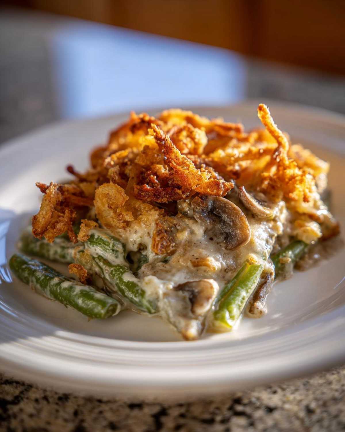 A close-up serving of creamy green bean casserole topped with crispy fried onions and mushrooms.
