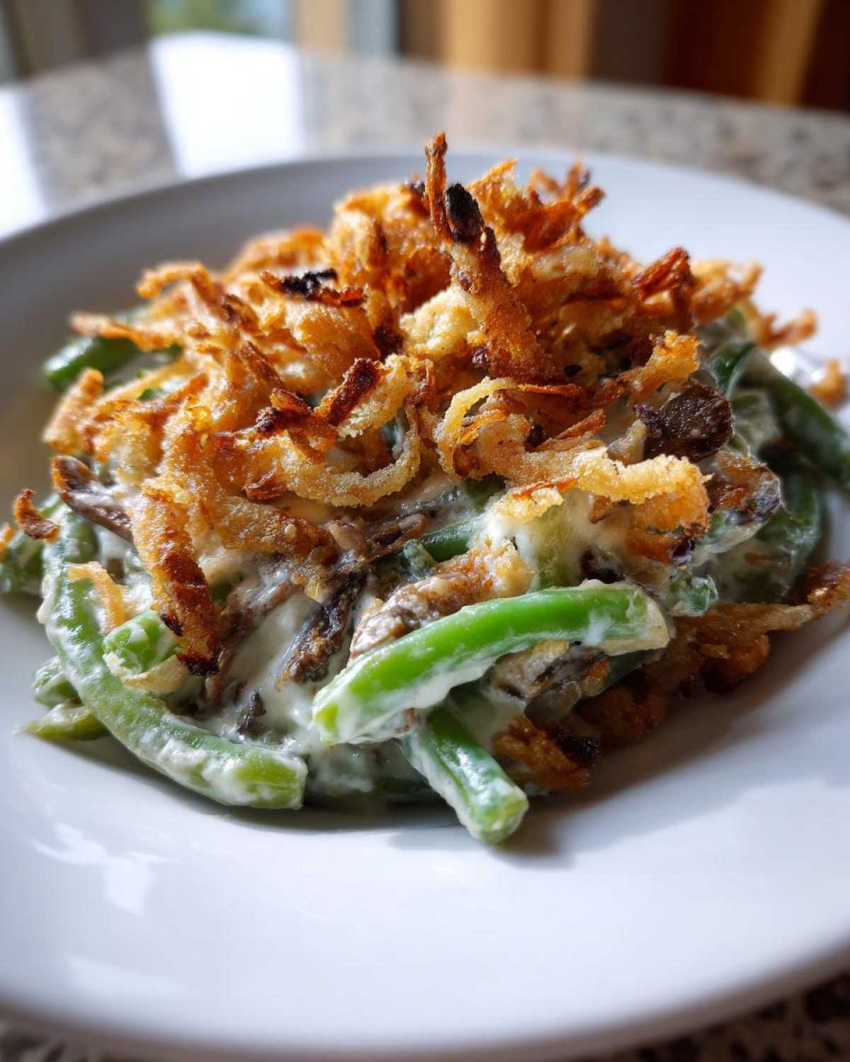 A close-up serving of classic green bean casserole, featuring bright green beans in a creamy sauce topped with crispy fried onions.