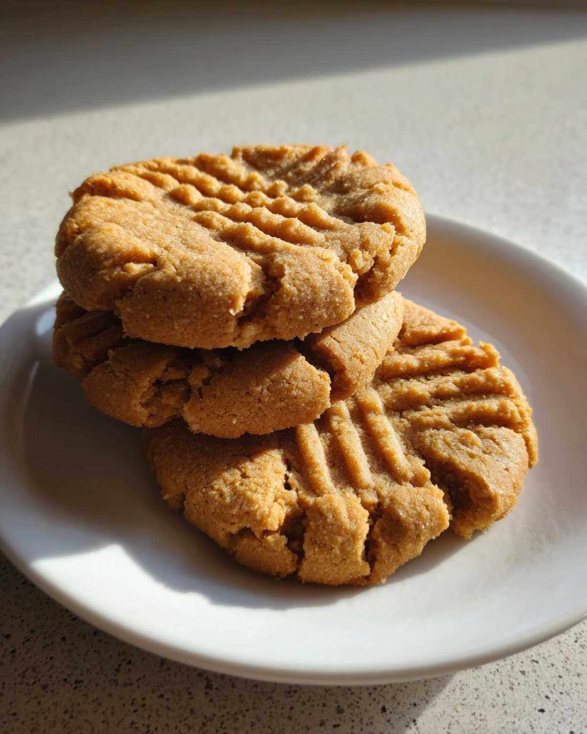 A close-up stack of three classic peanut butter cookies showing the traditional crisscross fork marks on a white plate.