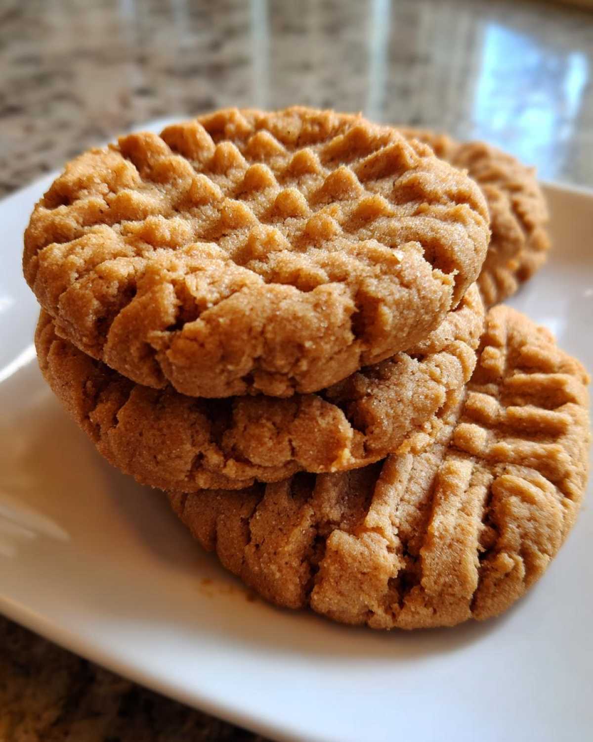 Close-up of three stacked, golden brown peanut butter cookies showing classic crosshatch fork marks.