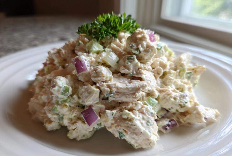 A mound of creamy cottage cheese chicken salad mixed with red onion and celery, garnished with parsley.