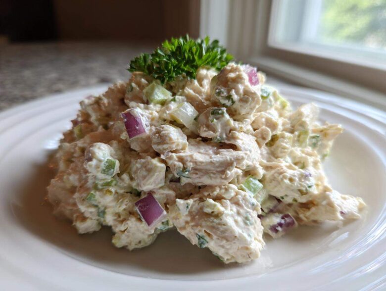 A mound of creamy cottage cheese chicken salad mixed with red onion and celery, garnished with parsley.