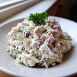 A mound of creamy cottage cheese chicken salad mixed with celery and red onion, garnished with parsley.