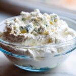 Close-up of a creamy blue cheese dip in a glass bowl, topped with generous crumbles of blue cheese.