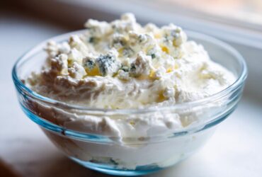 Close-up of a creamy blue cheese dip in a glass bowl, topped with generous crumbles of blue cheese.