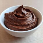 A close-up of rich, creamy chocolate dip swirled high in a small white bowl.