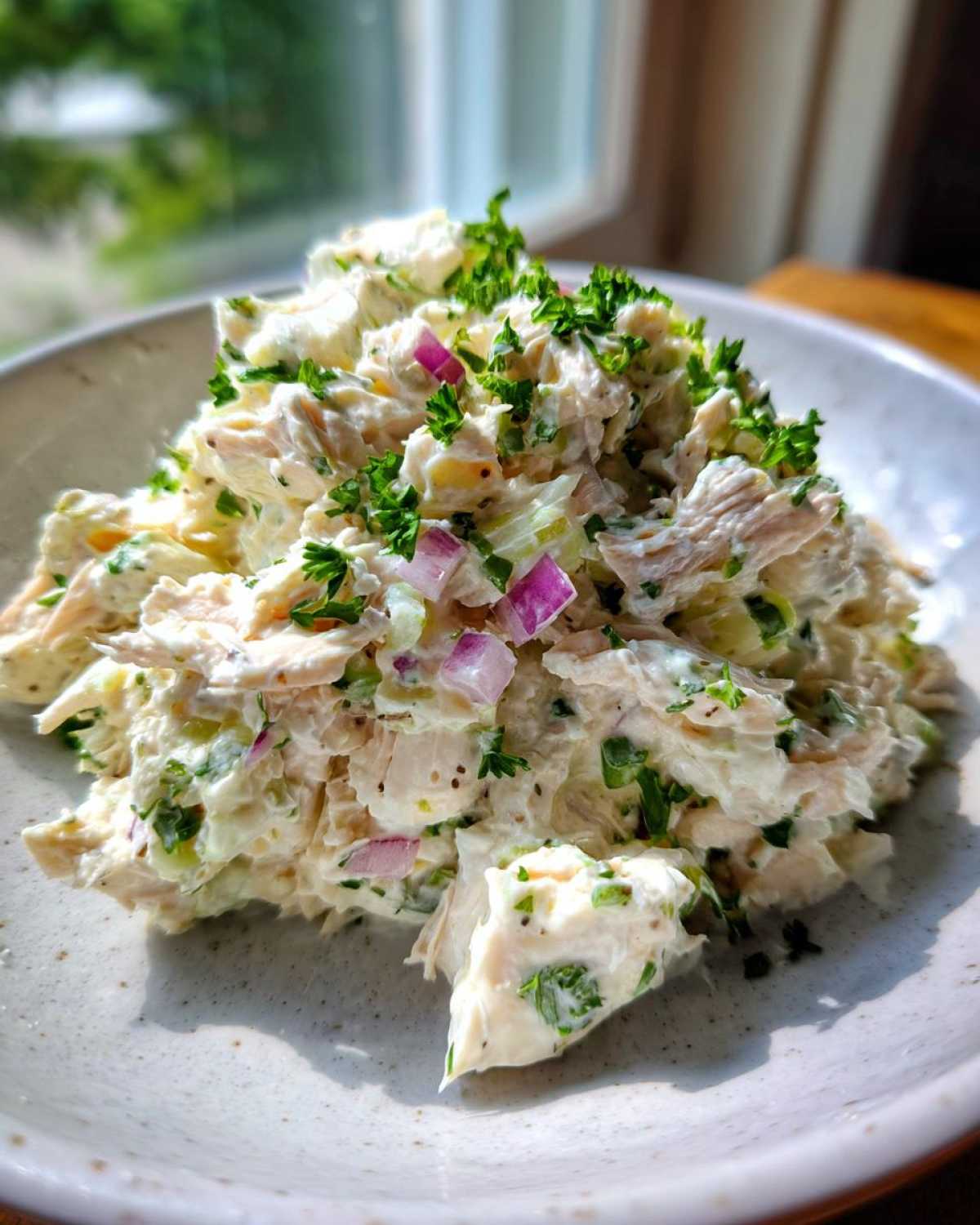 A mound of creamy cottage cheese chicken salad mixed with celery and red onion, topped with fresh parsley.