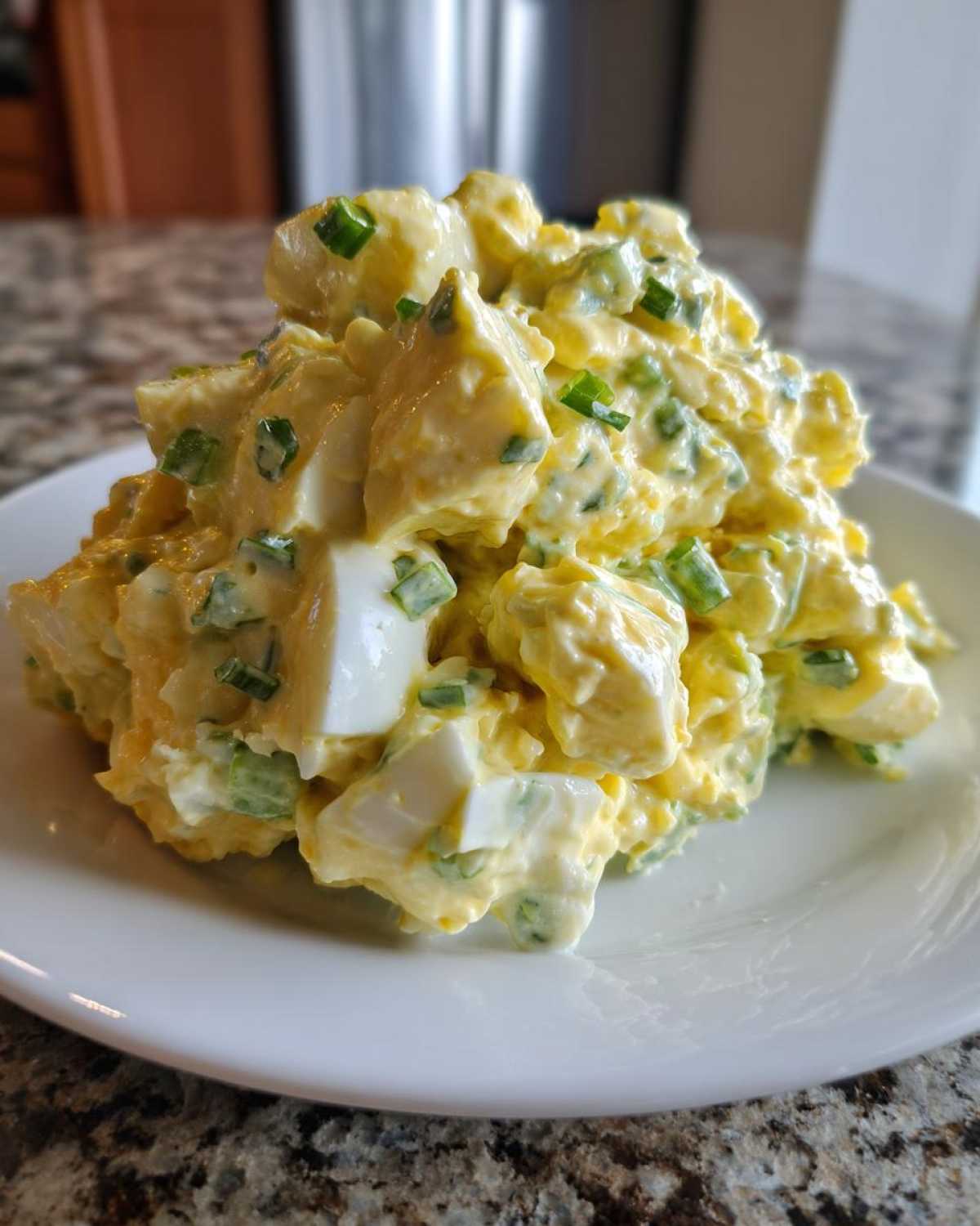A mound of creamy, chunky egg salad recipe mixed with mayonnaise and topped with fresh chopped green chives on a white plate.