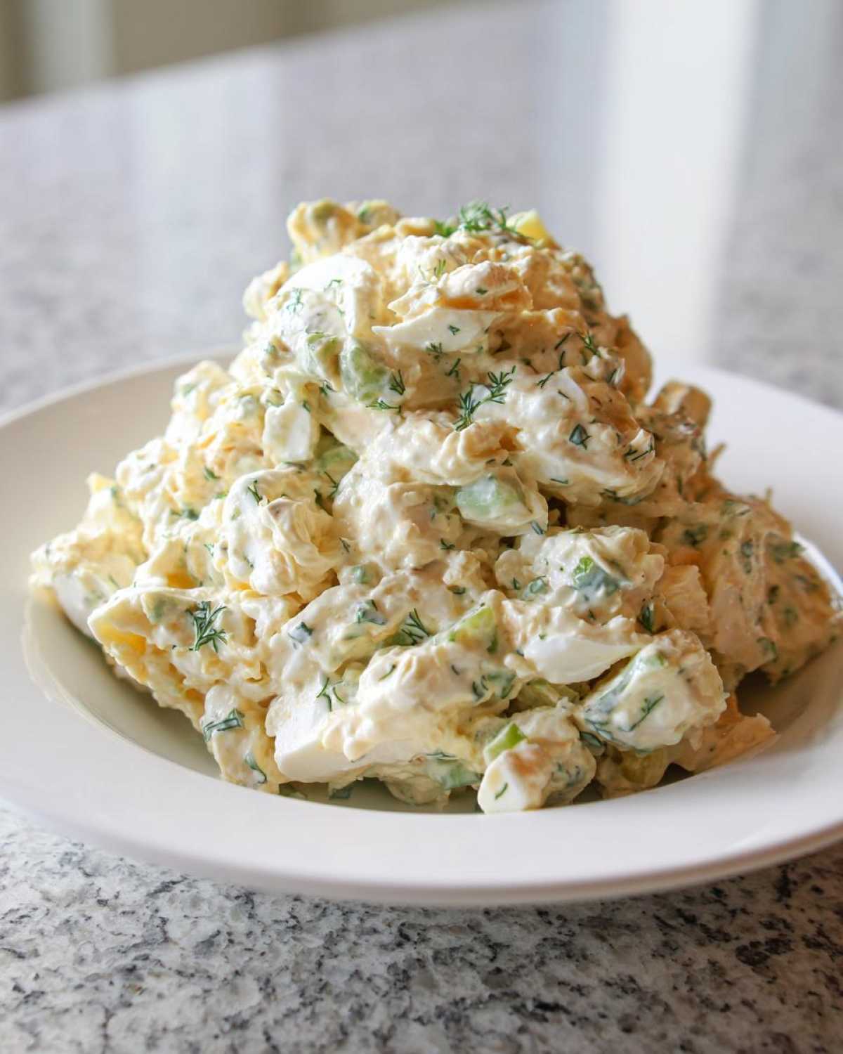 A generous mound of creamy egg salad recipe garnished with fresh dill, served on a white plate.