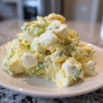A close-up of a mound of creamy egg salad recipe featuring chopped eggs, celery, and herbs on a white plate.