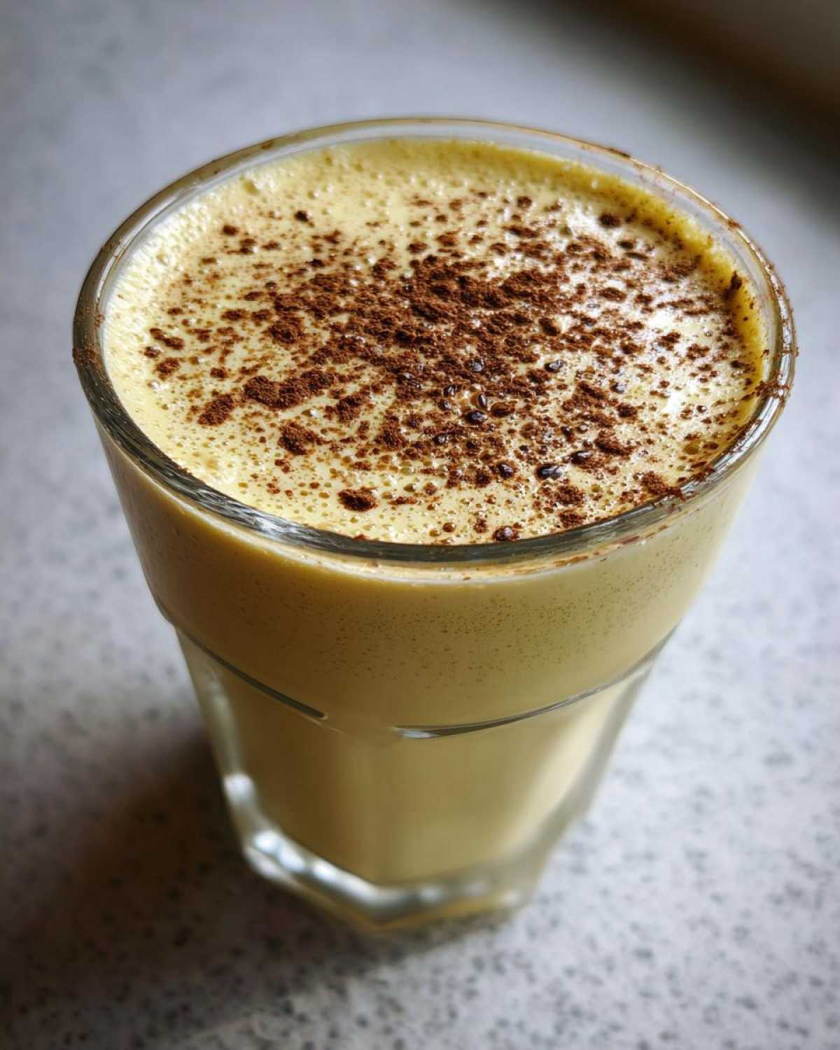 Close-up of a glass filled with creamy, yellow eggnog topped with a generous dusting of cinnamon.