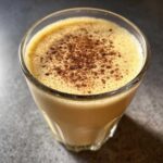 Close-up of a glass filled with creamy, frothy homemade eggnog, topped with a dusting of nutmeg.
