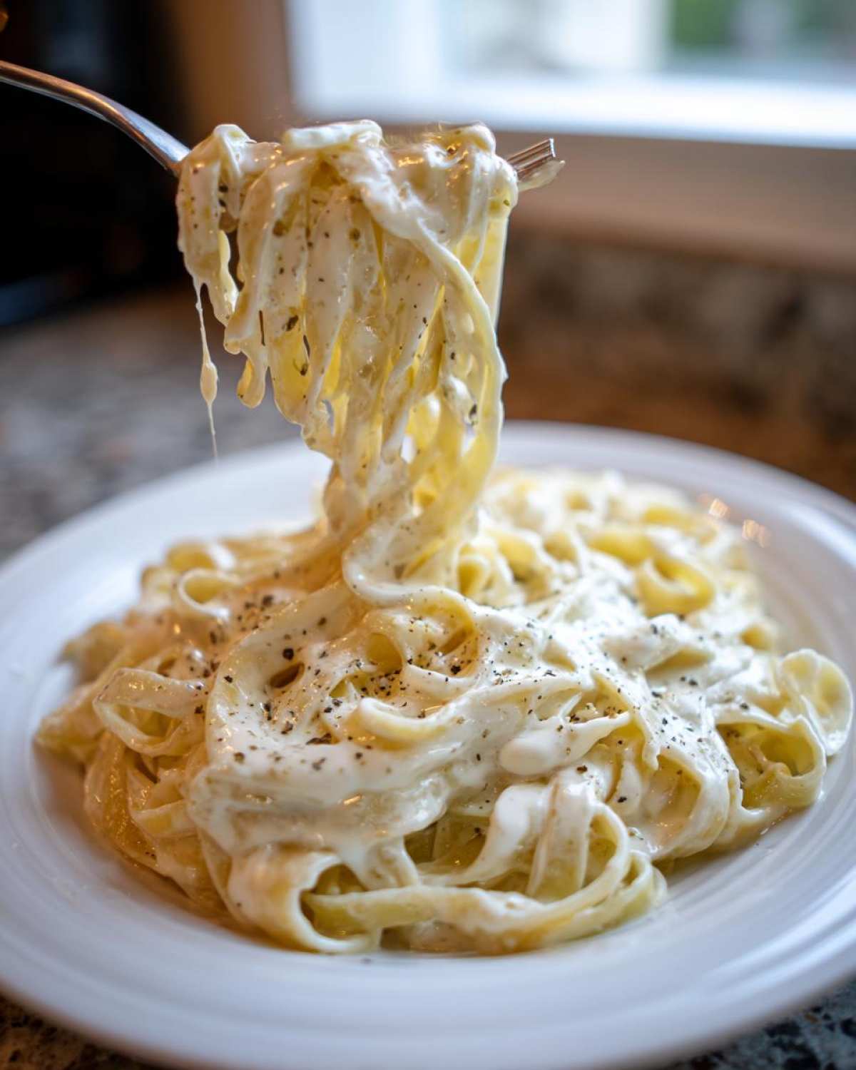 A fork lifting fettuccine noodles coated thickly in creamy homemade alfredo sauce, sprinkled with black pepper.
