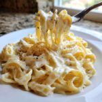 Close-up of fettuccine pasta coated in rich homemade alfredo sauce, lifted by a fork.