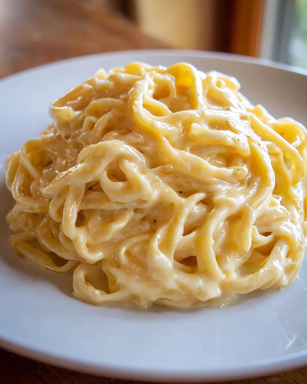 Close-up of fettuccine pasta drenched in rich, creamy olive garden alfredo sauce on a white plate.