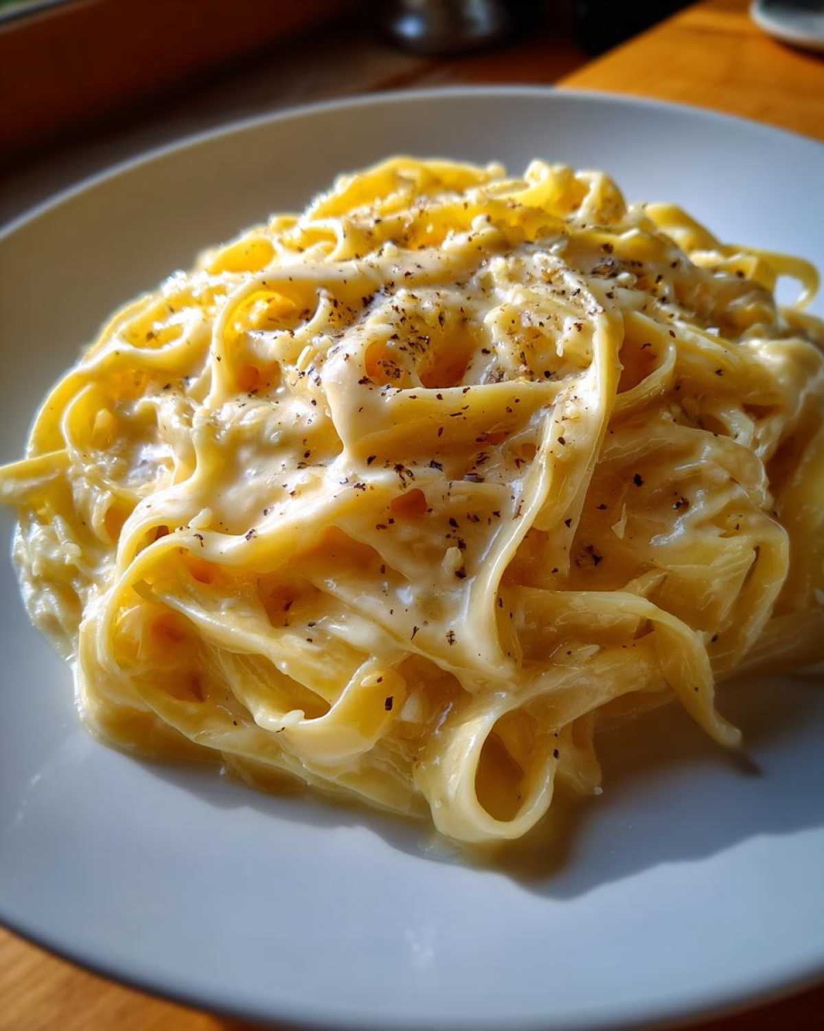 Close-up of fettuccine pasta coated in rich, creamy olive garden alfredo sauce and topped with black pepper.